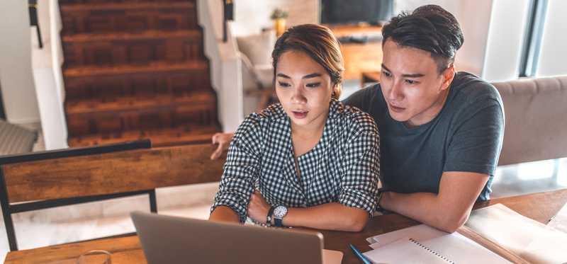 Two people appear serious while looking at laptop.