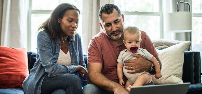 Two people looking at laptop while one holds baby.