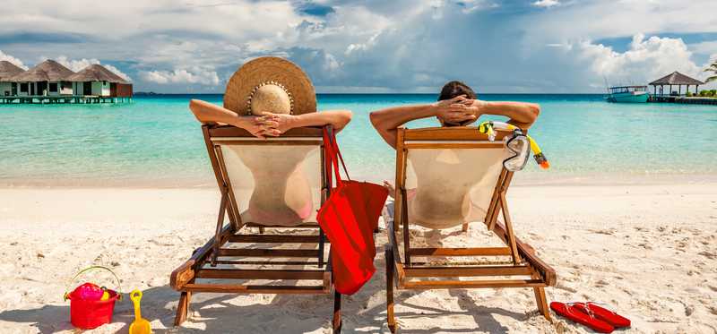 Two people sit together on chairs at the beach.