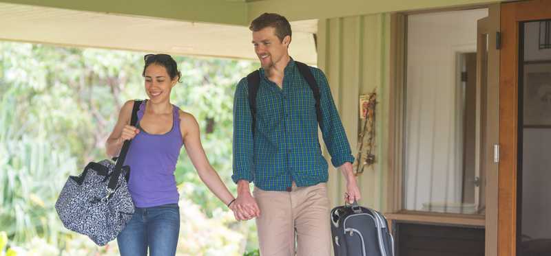 Two people carrying luggage and walking outside a vacation house.