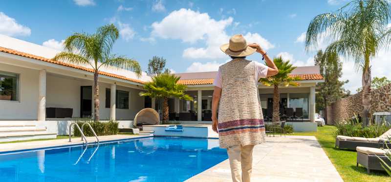 Person walking alongside a pool in the backyard of a home.