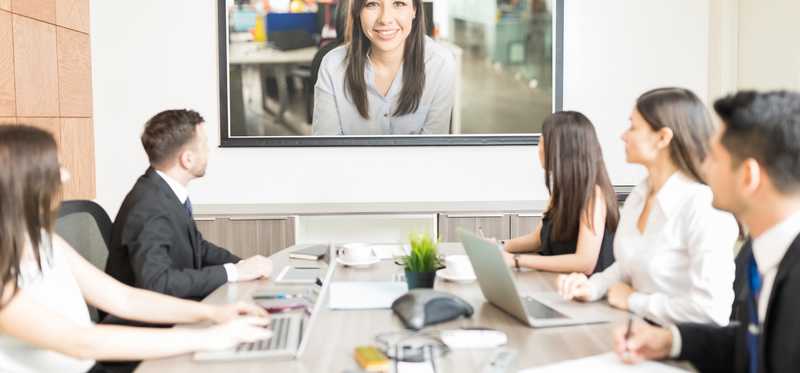 Businesspeople sitting around a conference table looking at a video screen