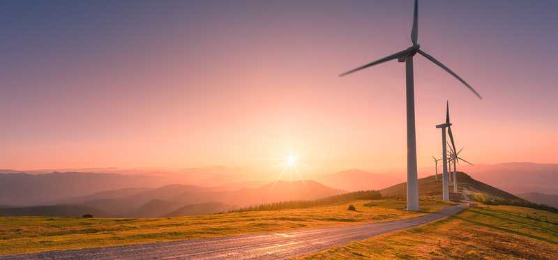 Wind turbines along a road with the sun setting in the background.
