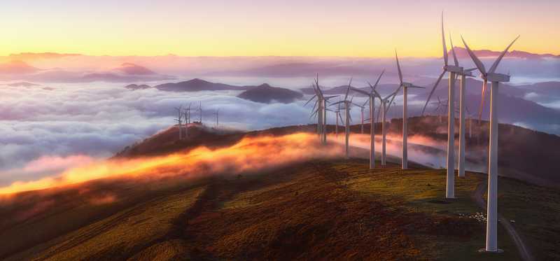 Wind turbines on the top of a mountain with fog below.