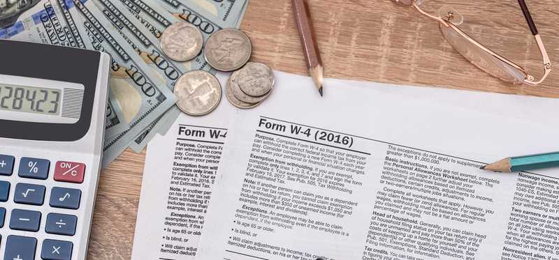 Tax forms with cash, calculator, glasses, and pencils.
