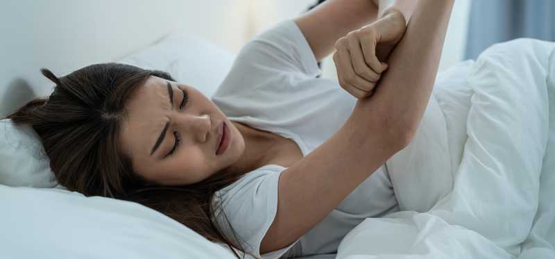Person lying in bed and scratching bug bites.