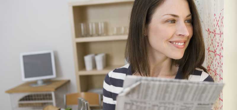 A smiling woman holding a financial newspaper and looking off into the distance.