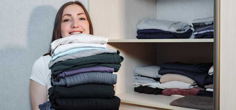Woman holding stack of clothing in a closet