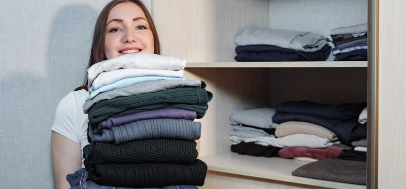 Person holding stack of clothing from a closet.
