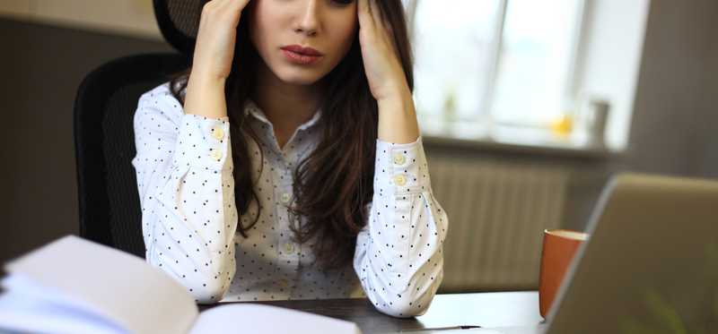 Woman holding head looking stressed with books and laptop