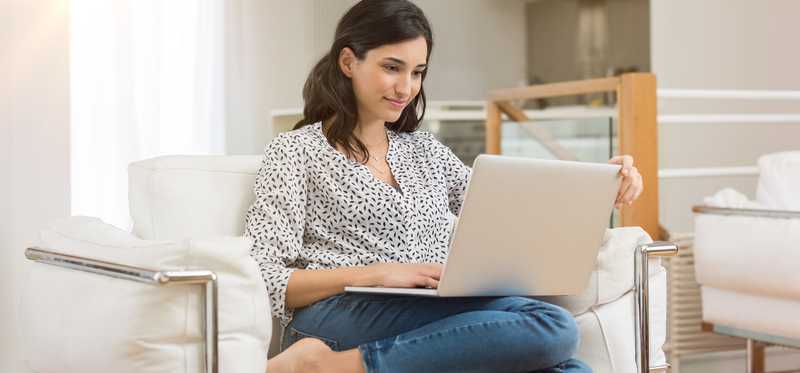 A person sits on a chair while working on a laptop.