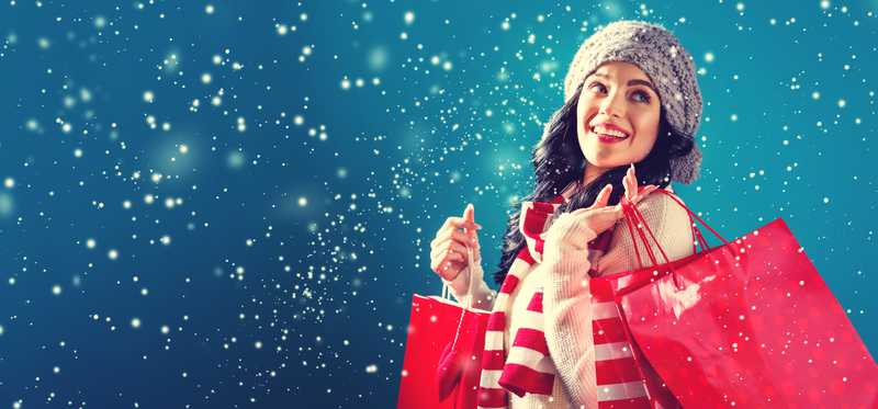 Woman standing outdoors with snow falling holding shopping bags.