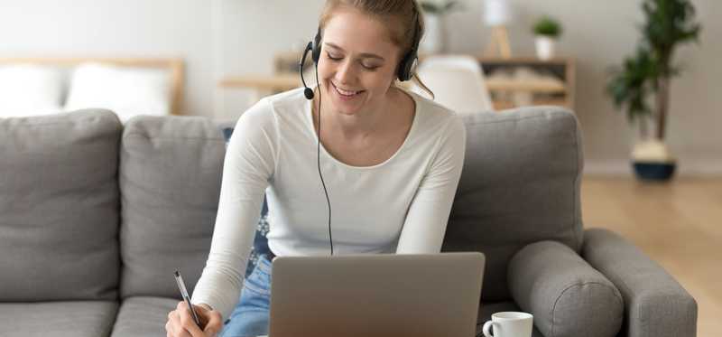 Woman with headphones and laptop writing a note