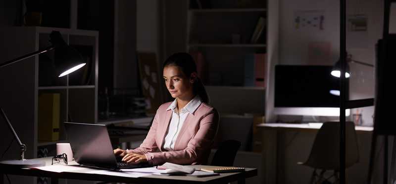 Person working on laptop at night in dark office.