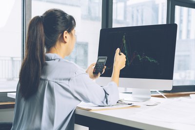 Women using calculator while looking at stock chart on computer screen