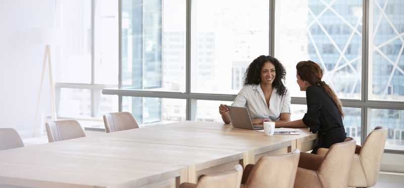 Two women talk at a conference table.