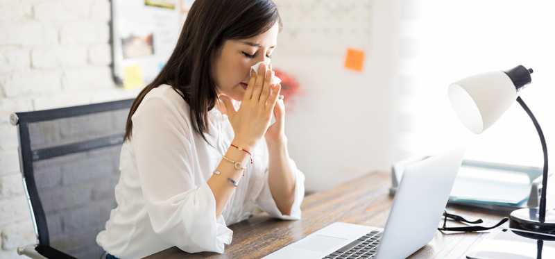 A woman works while holding a tissue to her nose.