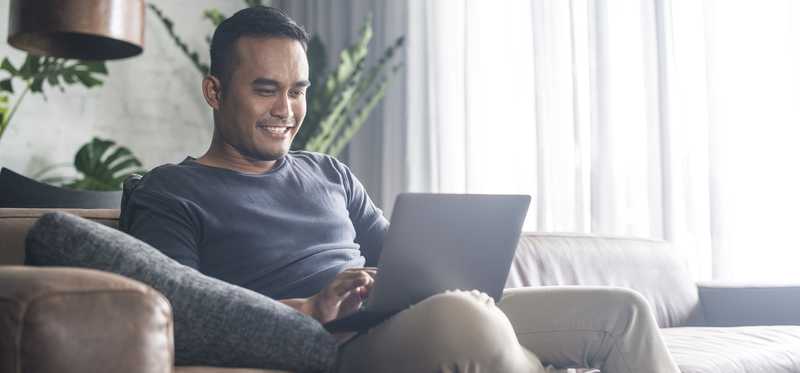 A person sits with a laptop on a couch.