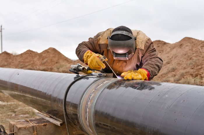 Worker in protective gear welding a gas pipe outdoors