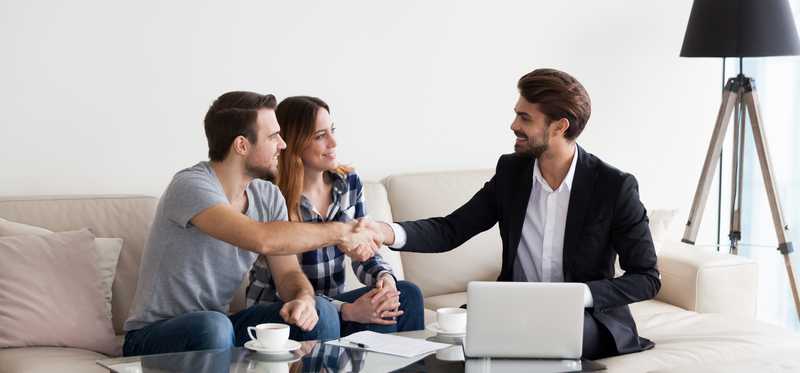 Young couple shaking hands with businessman in home