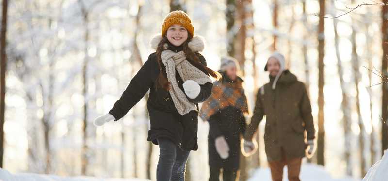 Person running in snow while their parents walk behind them.