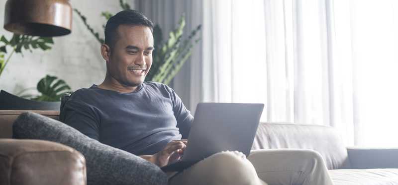 Person smiling on laptop and sitting on couch.