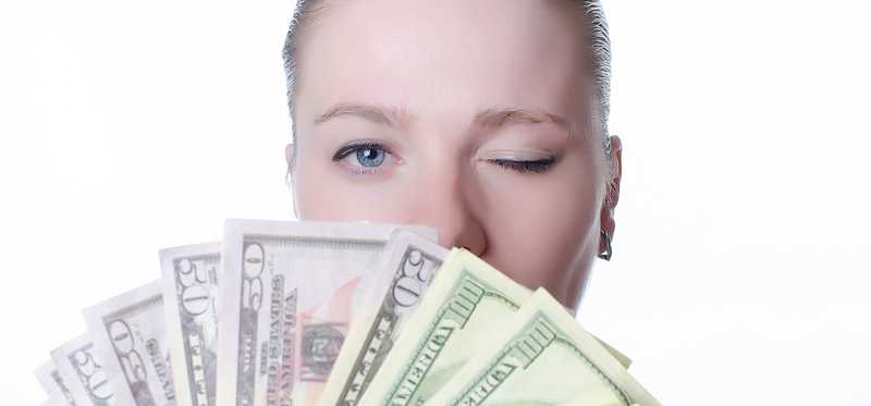 Young woman holding a fan of cash and winking.