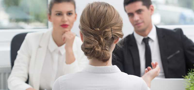 Young woman sitting across from two other people all in business attire.