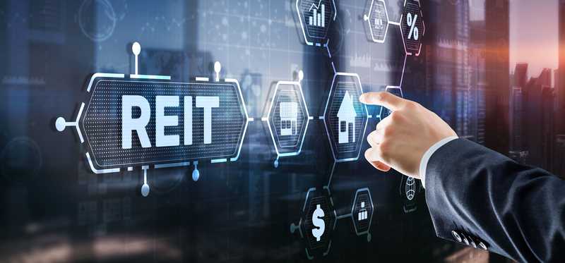 A hand pointing at a digital board that says REIT.
