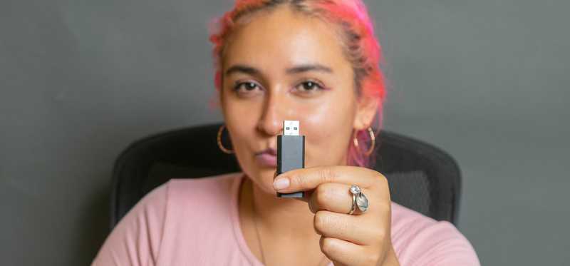 Adult with pink hair holds up USB drive.