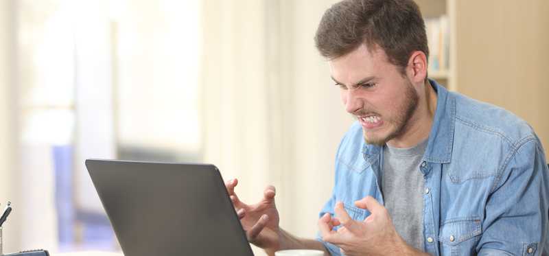 Person clenching hands while making angry expression at laptop.