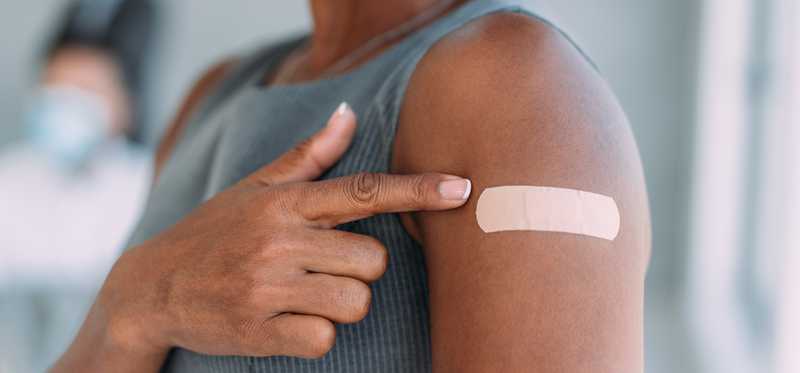 Person pointing to bandage on their arm.