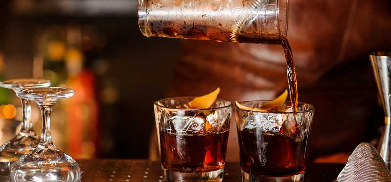 Two drinks are being poured into glasses at a bar.