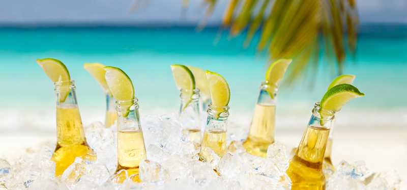 Beers with lime in ice with beach in the background.
