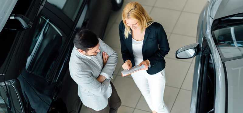 Woman and man standing in a car showroom looking at paperwork.