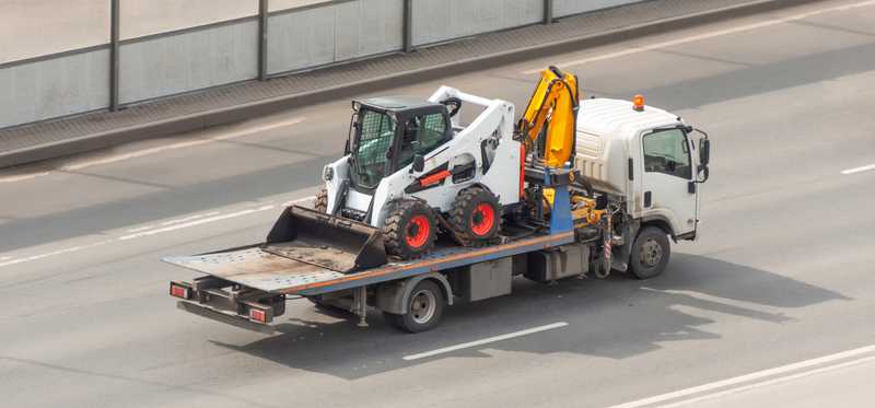Bobcat construction vehicle being hauled by truck.