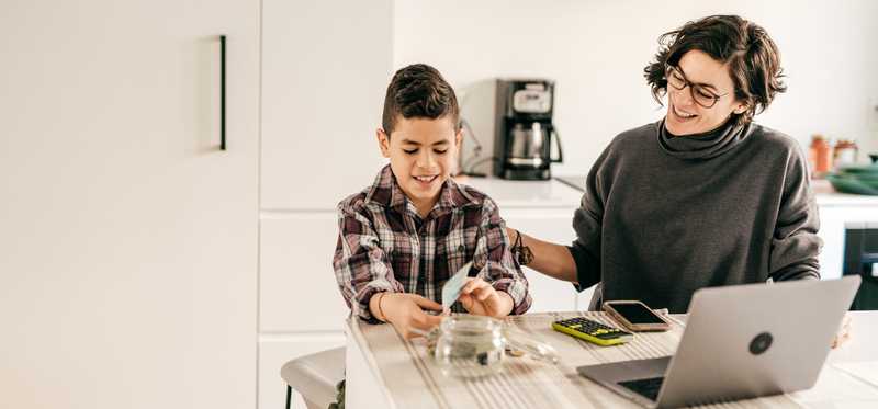 Child counts cash in front of glass jar while adult smiles.