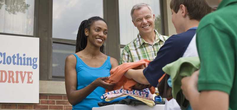 Child handing some clothes to an adult at a clothing donation event.
