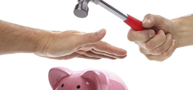 A piggy bank with a hand outstretched above it, stopping it from being smashed by a hammer.
