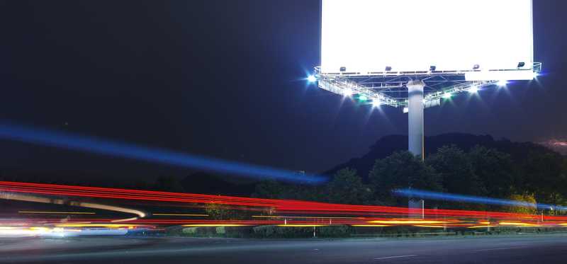 A brightly lit blank digital billboard on a busy highway at night.