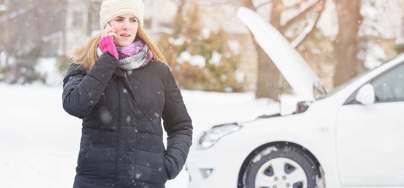 Woman in coat on cell phone in front of car with its hood up