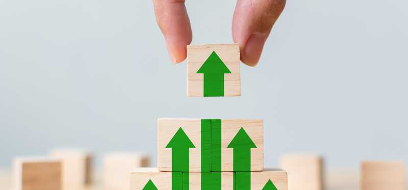 Hand building blocks with green up arrows.
