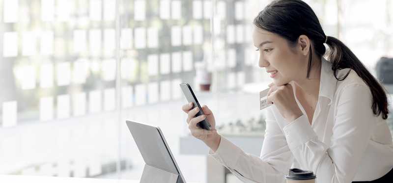 Person holding smartphone and credit card while sitting at office desk.