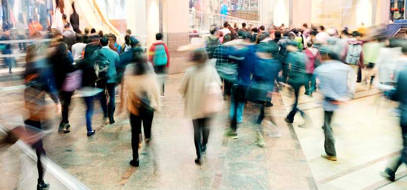The inside of a busy retail mall with people walking through as blurs.