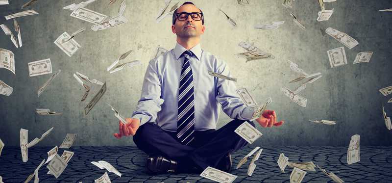 Man in meditation pose as money floats around him.