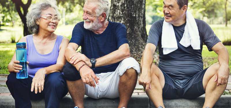 Three older people sitting on the curb of a road after a workout.