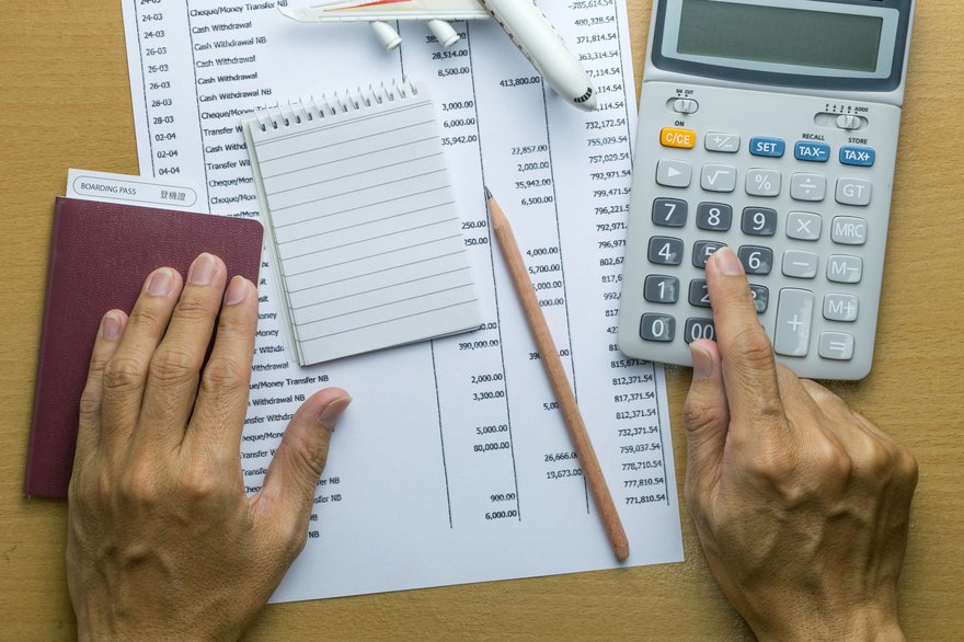 Hands sit on top of paperwork while using a calculator and taking notes.