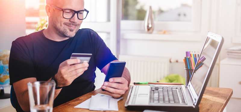 A person is holding a credit card and smartphone while sitting in front of a laptop.