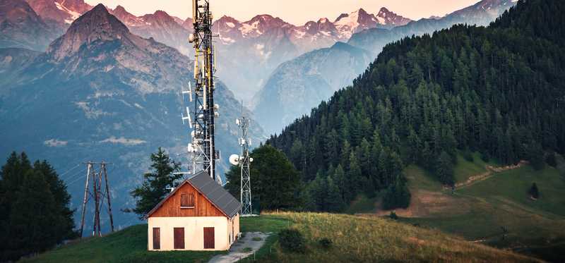 A striking shot of a cabin and cell towers in front of snowy peaks.