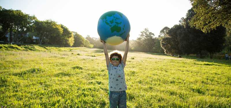 Child standing outside holding globe above head.